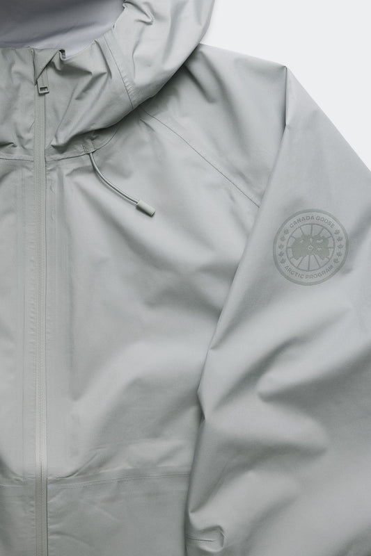 Close up of a light grey hooded jacket with a compass-like logo on the sleeve.