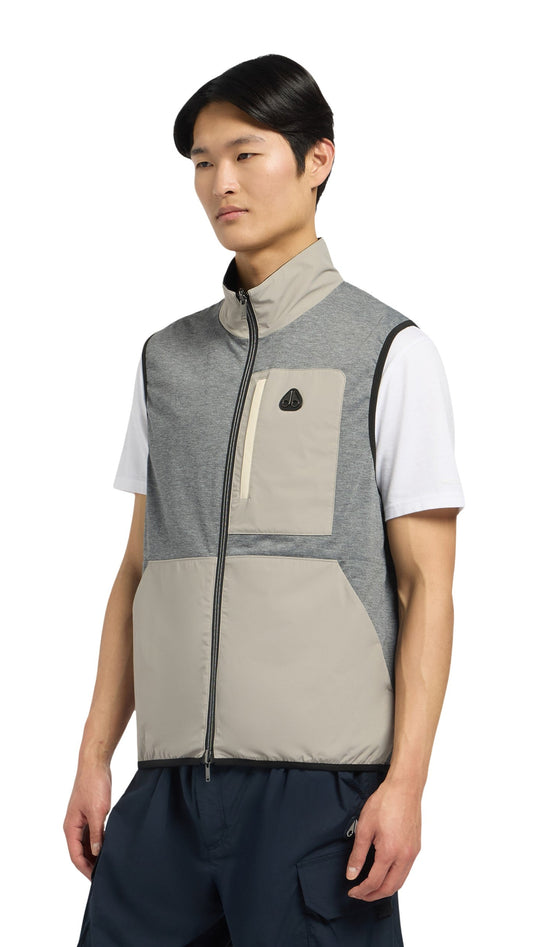 A man wearing a grey and beige sleeveless zip-up vest, with a small logo on the left breast pocket.