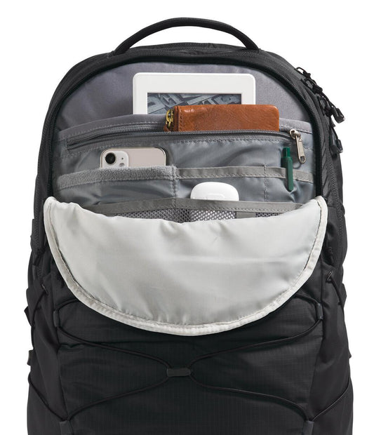 Open black backpack showing internal mesh pockets containing an e-reader, wallet, phone, and earbuds.
