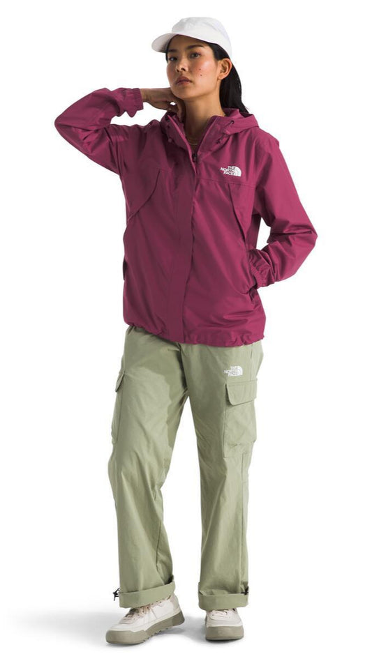 A person wearing a white cap, a magenta jacket, and olive-green cargo pants stands and looks into the distance.