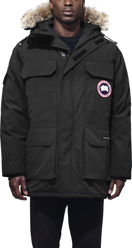 Person wearing a black parka with a fur-trimmed hood and several pockets. A circular patch with a design is on the upper arm.