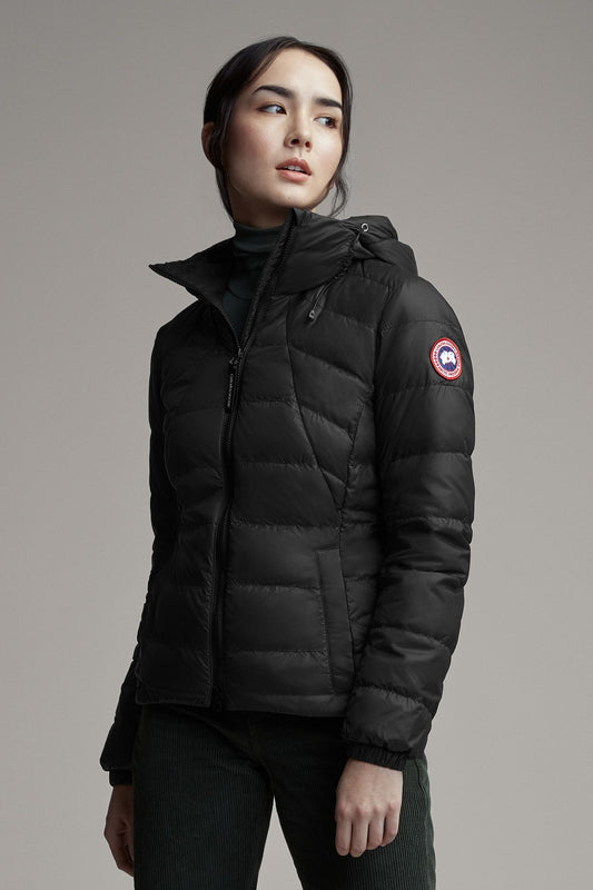 A woman wearing a black puffer jacket with a hood and the company's logo on the sleeve.