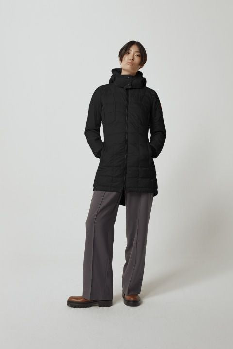 A woman in a long, black, puffy jacket with a hood, dark gray slacks, and brown leather shoes.