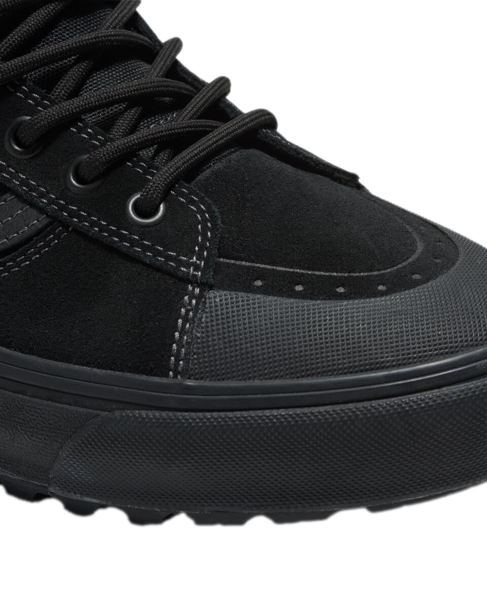 Close-up of a black shoe, featuring a suede upper, black laces, and a textured toe cap.