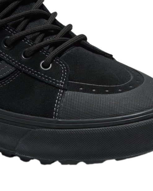 Close-up of a black shoe, featuring a suede upper, black laces, and a textured toe cap.