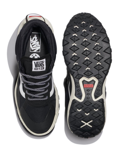 Overhead view of two sneakers. The left sneaker shows a black upper with a white side stripe, black and white laces and black tongue with a white Vans patch. The right sneaker shows the sole with a black and white tread with a red text detail.