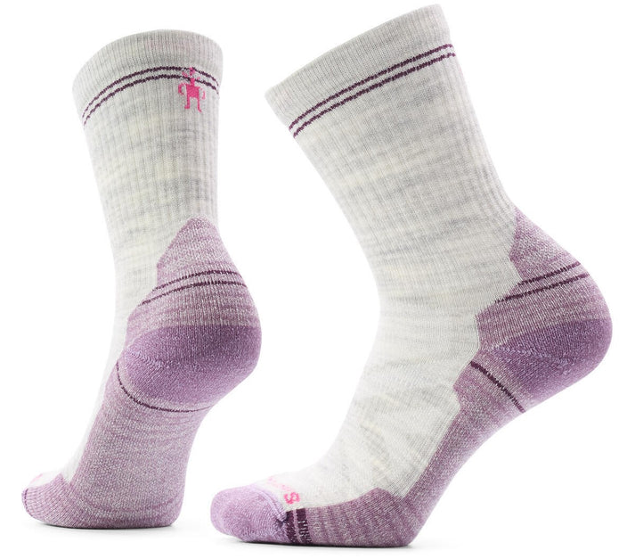 A pair of light heather grey crew-length hiking socks with lavender-colored heels, toes, and arch support panels. The socks feature a subtle textured knit pattern and a small pink logo embroidered near the top cuff.