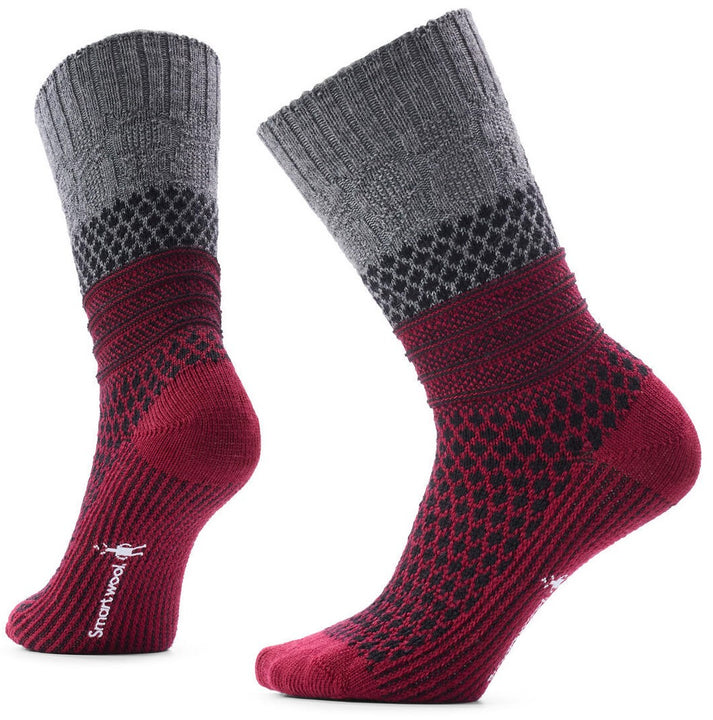 A pair of Smartwool brand mid-calf socks with a decorative pattern, featuring a grey ribbed cuff, a black and grey diamond pattern section, followed by a ribbed band and a burgundy foot area with a textured knit finish and the Smartwool logo printed on the side.
