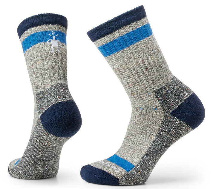 A pair of heather grey wool hiking socks featuring a dark navy blue toe and heel, a dark navy blue cuff, and a bright blue horizontal stripe near the top of the calf and across the arch of the foot; the side of the calf features a small, white stylized hiker logo.