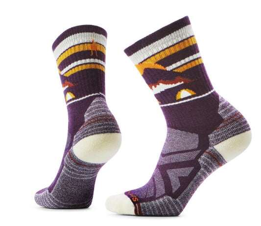 Two purple socks with white heels and toes featuring orange, brown, and white stripes with a mountain and camping scene design.