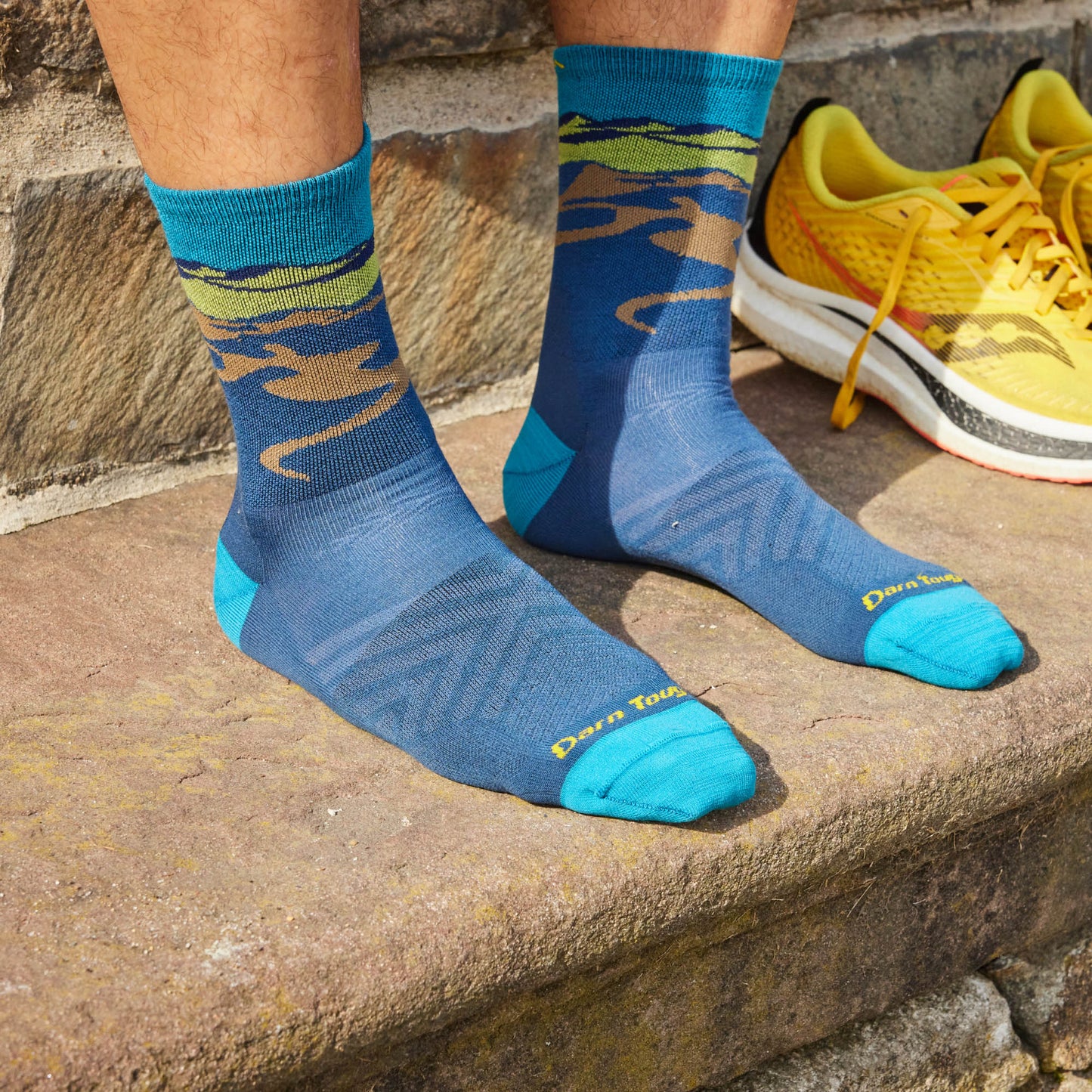 Person wearing blue patterned socks with teal toes, heels, and cuffs; next to yellow and white sneakers.