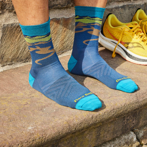 Person wearing blue patterned socks with teal toes, heels, and cuffs; next to yellow and white sneakers.