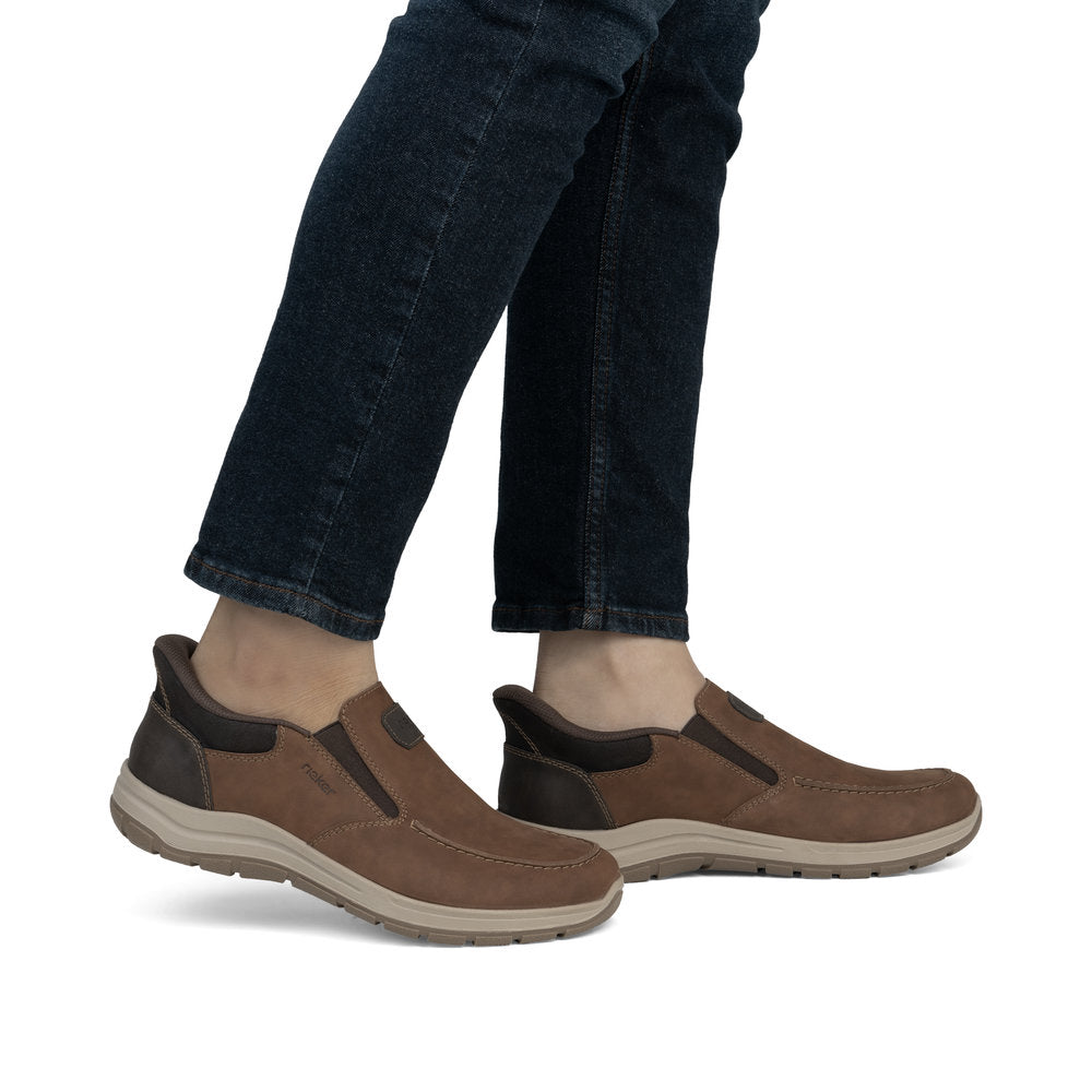 A person wearing brown leather slip-on shoes with dark blue jeans.