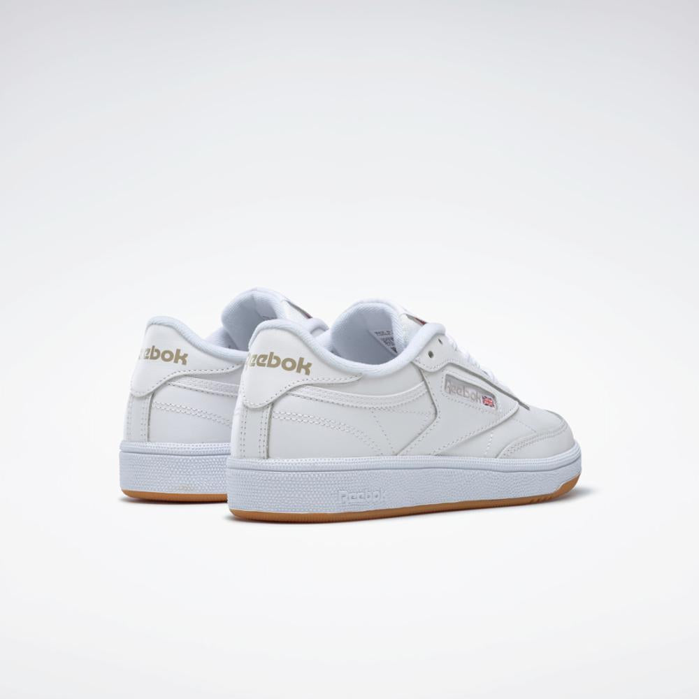 Pair of white leather sneakers with gum soles and gold-colored 'Reebok' printed near the heel.