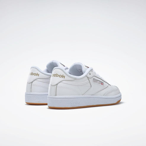 Pair of white leather sneakers with gum soles and gold-colored 'Reebok' printed near the heel.