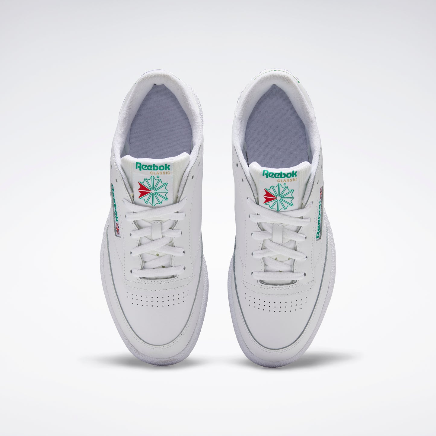 A pair of white low top sneakers with white laces, green and red logo on the side, and perforated toe box.