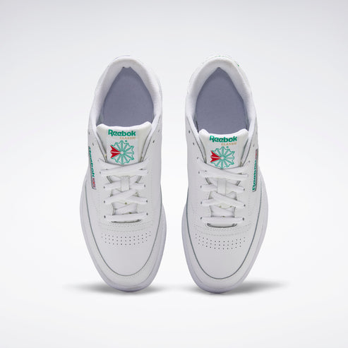 A pair of white low top sneakers with white laces, green and red logo on the side, and perforated toe box.