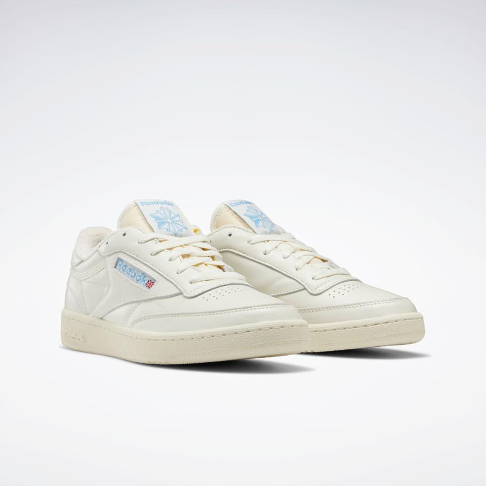 Off-white sneakers with light tan laces, and a retro Reebok logo on the side.