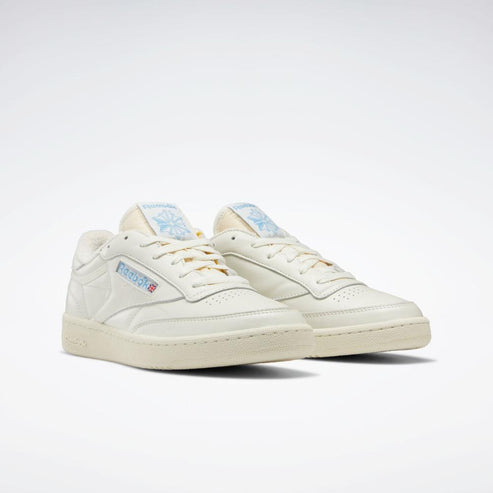 Off-white sneakers with light tan laces, and a retro Reebok logo on the side.