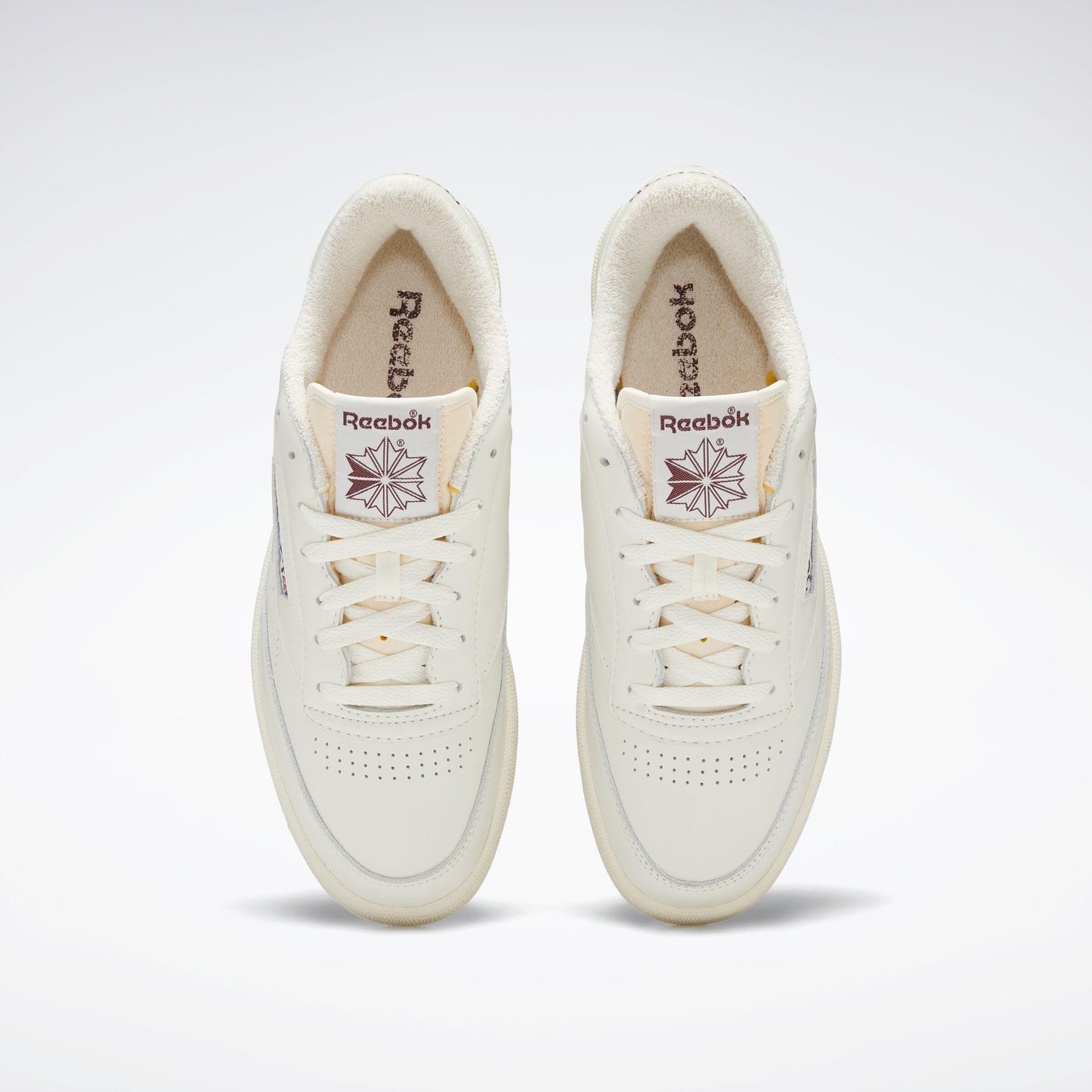 Top-down view of two off-white Reebok Club C 85 Vintage shoes. The interior is a tan color with the Reebok logo. The shoes are laced.