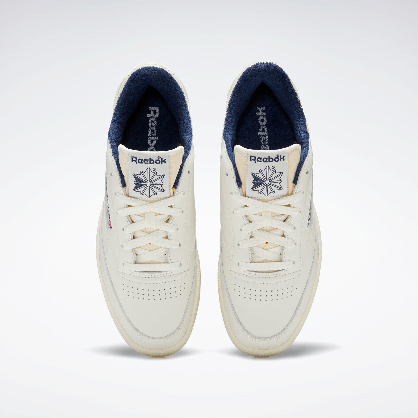 Pair of off-white sneakers with navy blue lining, perforated toe box and laces.
