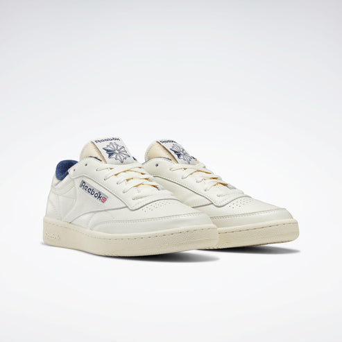 Cream-colored low top sneakers with gold laces and blue accents.