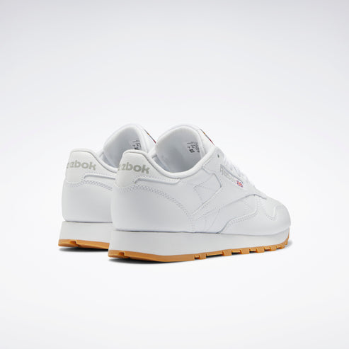 Low-cut white sneakers with tan soles and "Reebok" printed on the heel.