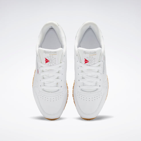 Top-down view of a pair of white sneakers with white laces and gum soles.  The tongue shows a logo with a red design.