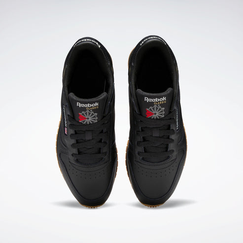 Overhead view of a pair of black sneakers with black laces and a red and grey flower logo on the tongue.