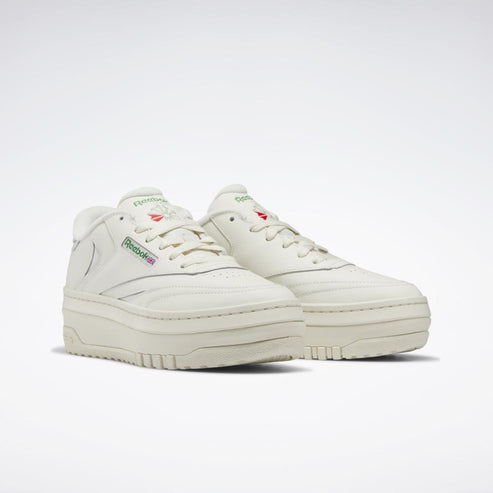 Platform tennis shoes in off-white with a round toe, white laces, and a red and green logo on the side.