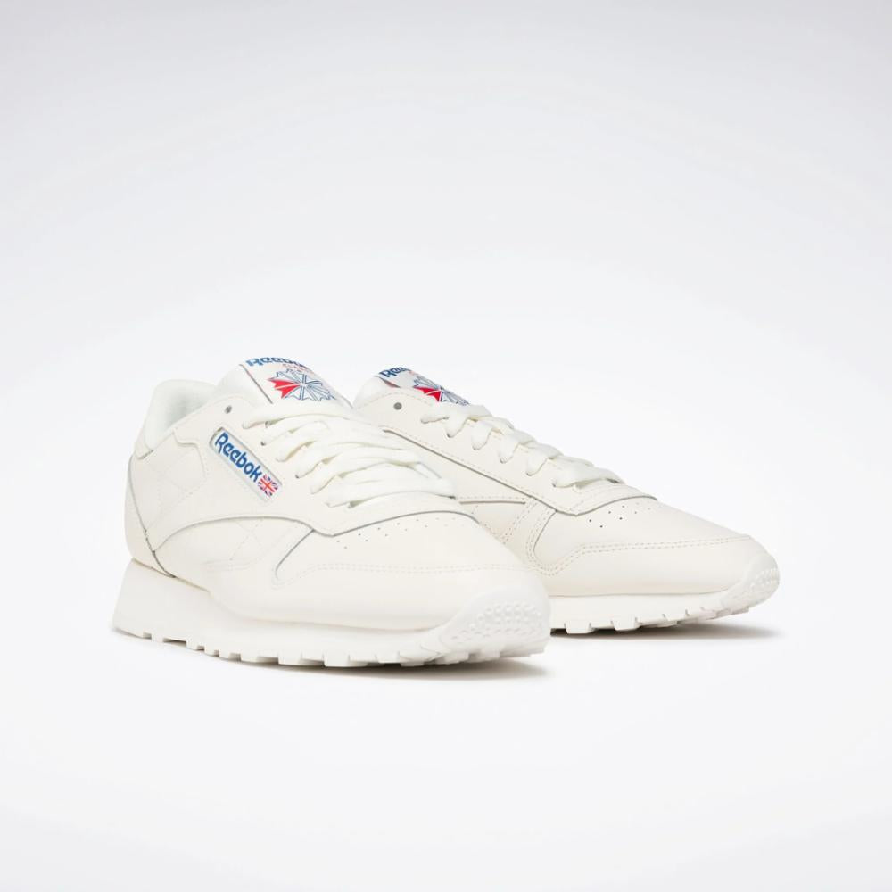 Pair of cream leather sneakers with perforated toe box, blue and red logos on the side and tongue.