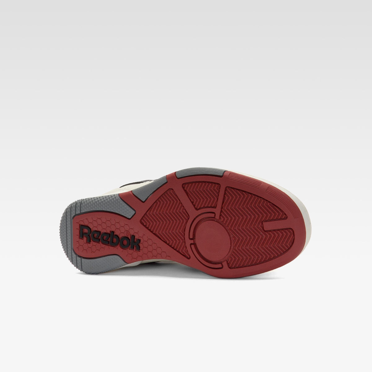 Bottom view of a shoe with a dark red sole, with the text "Reebok" in black printed at the heel.