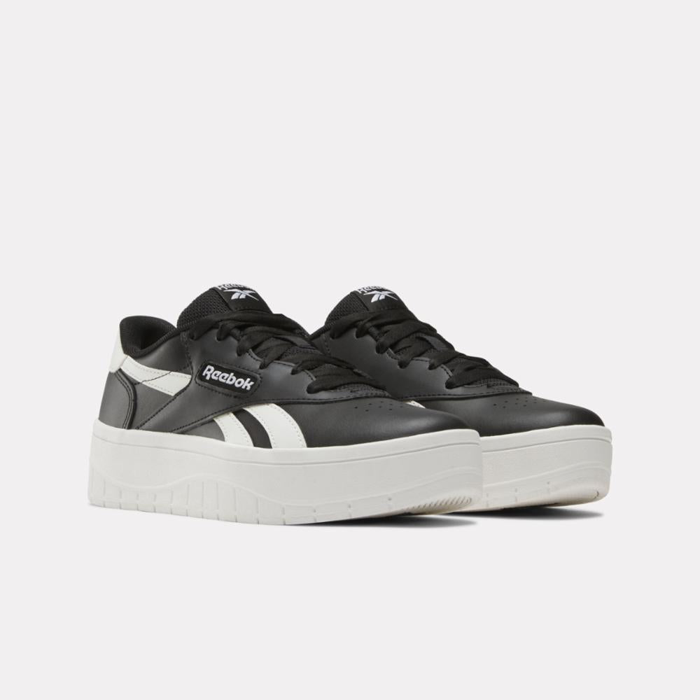 Low-top sneakers with platform soles, black with white stripe, "Reebok" logo.