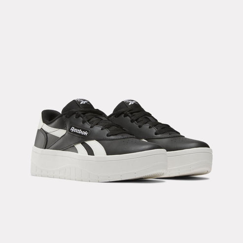 Low-top sneakers with platform soles, black with white stripe, "Reebok" logo.