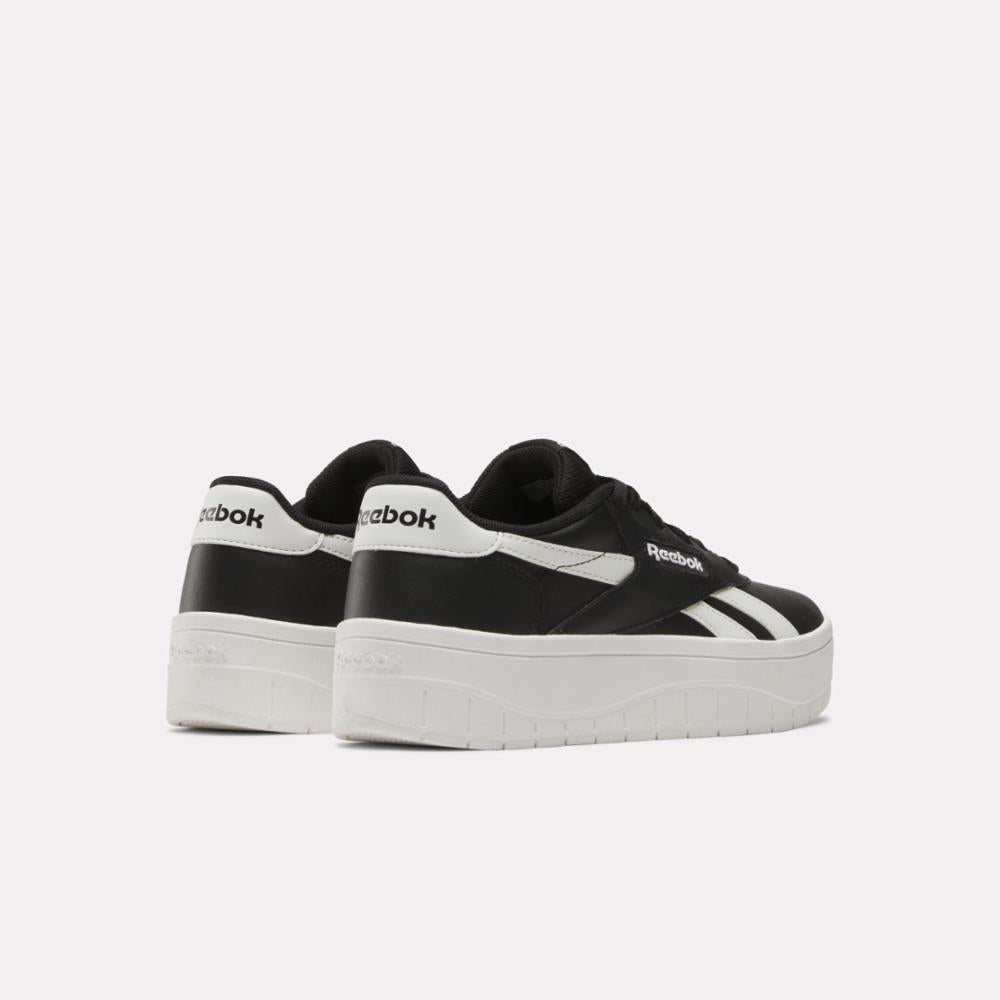 Pair of black and white sneakers with thick white soles, heel and side logo.