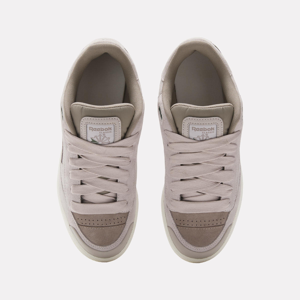 Overhead view of two beige sneakers with white laces. The tongue of each shoe has a Reebok logo.