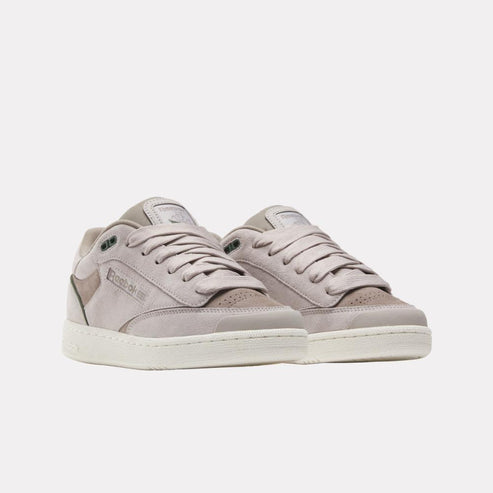 Two low-top sneakers with shades of gray, featuring laces, leather/suede design and a logo on the side of each sneaker.