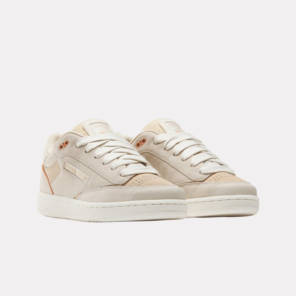 Pair of low-top sneakers in cream color, featuring white laces and light brown accents.
