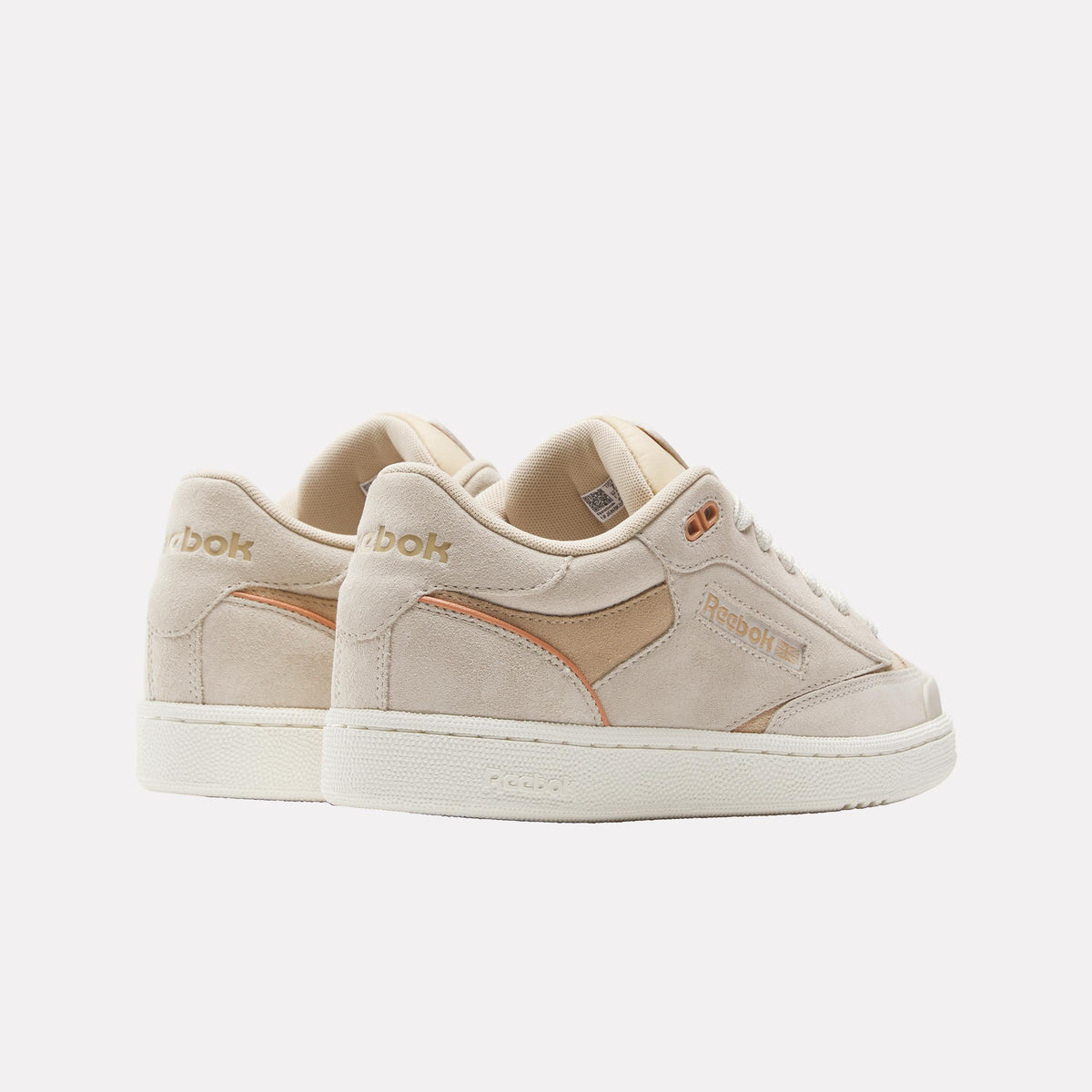 Two low-top sneakers, each with tan suede and nylon body, white sole, and "Reebok" written in gold font.