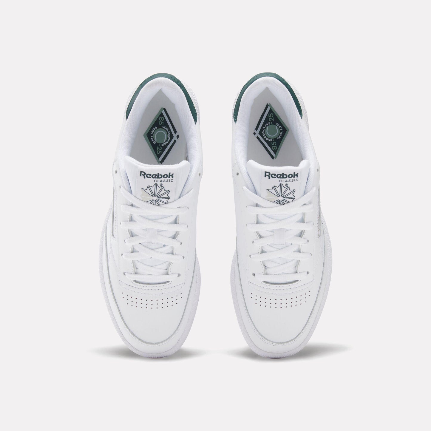 Two white sneakers with green accents, laces and perforated toeboxes are visible.