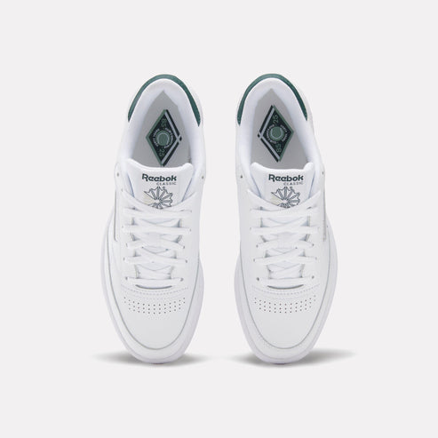 Two white sneakers with green accents, laces and perforated toeboxes are visible.