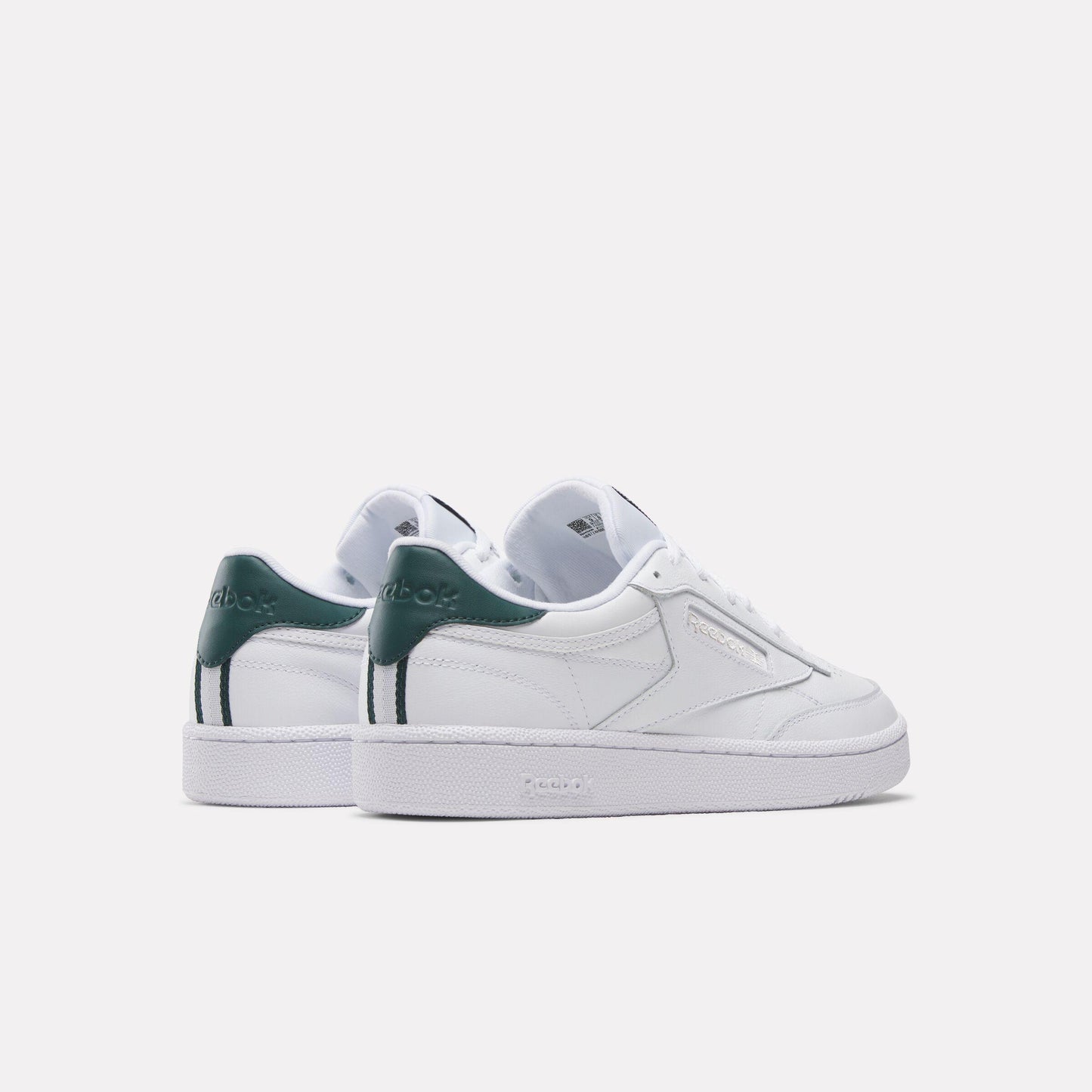 Low-top white sneakers with green accents on the heel and a flat sole, viewed from the back.