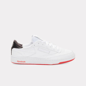 A white low-top sneaker with a black heel and a red sole with the word "Reebok" written on it.
