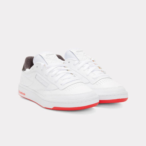 Pair of white sneakers with red soles, laces and a brown interior.