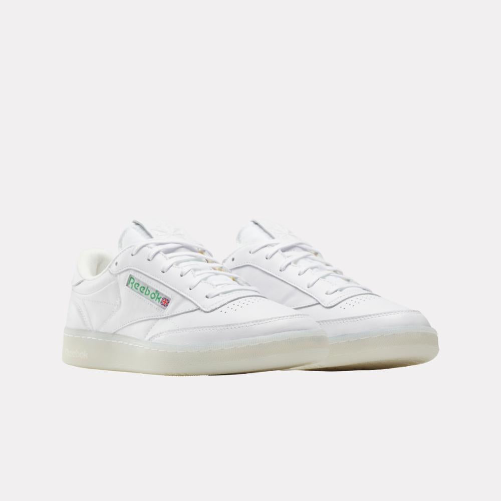 White low-top sneakers with a translucent sole and green logo on side.