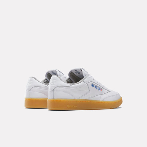 A pair of white leather sneakers with gum soles, side view, logo with blue lettering.