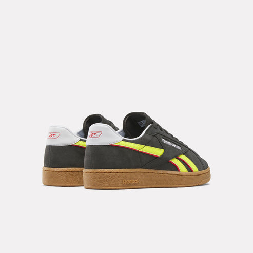 Low profile black sneaker with a gum sole, yellow and red stripes, and a white and red logo on the heel.