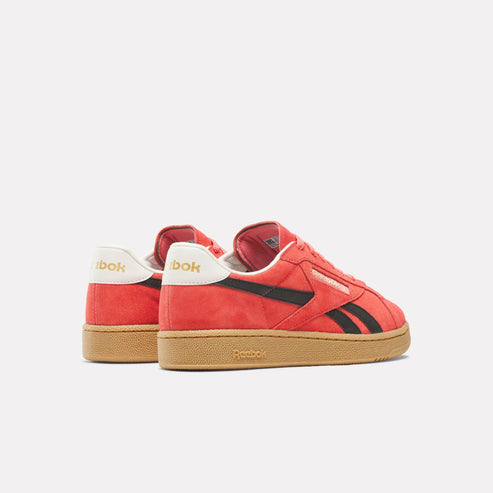 A pair of coral low-rise suede sneakers with black stripes and white heel tabs, bearing the word “bok” and resting on gum soles.