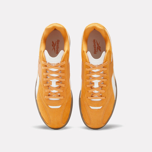 Overhead view of two matching tangerine colored suede sneakers with white laces and Reebok logo inside.