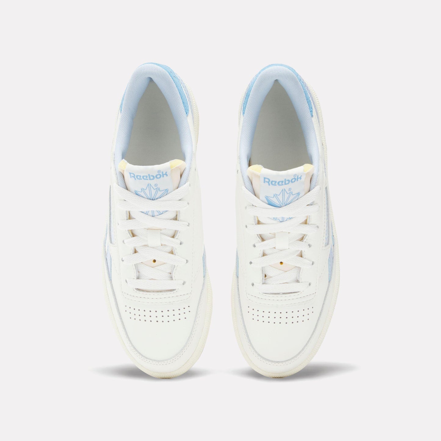 Overhead view of two white leather sneakers with white laces and light blue accents on the heel and tongue lining.
